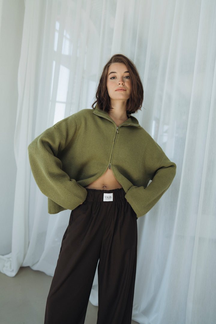 Grüner Cardigan aus weichem Strick. Oversized geschnitten mit Stehkragen und weiten Ärmeln. Der Cardigan hat einen Reißverschluss, der sich von unten und oben öffnen lässt.