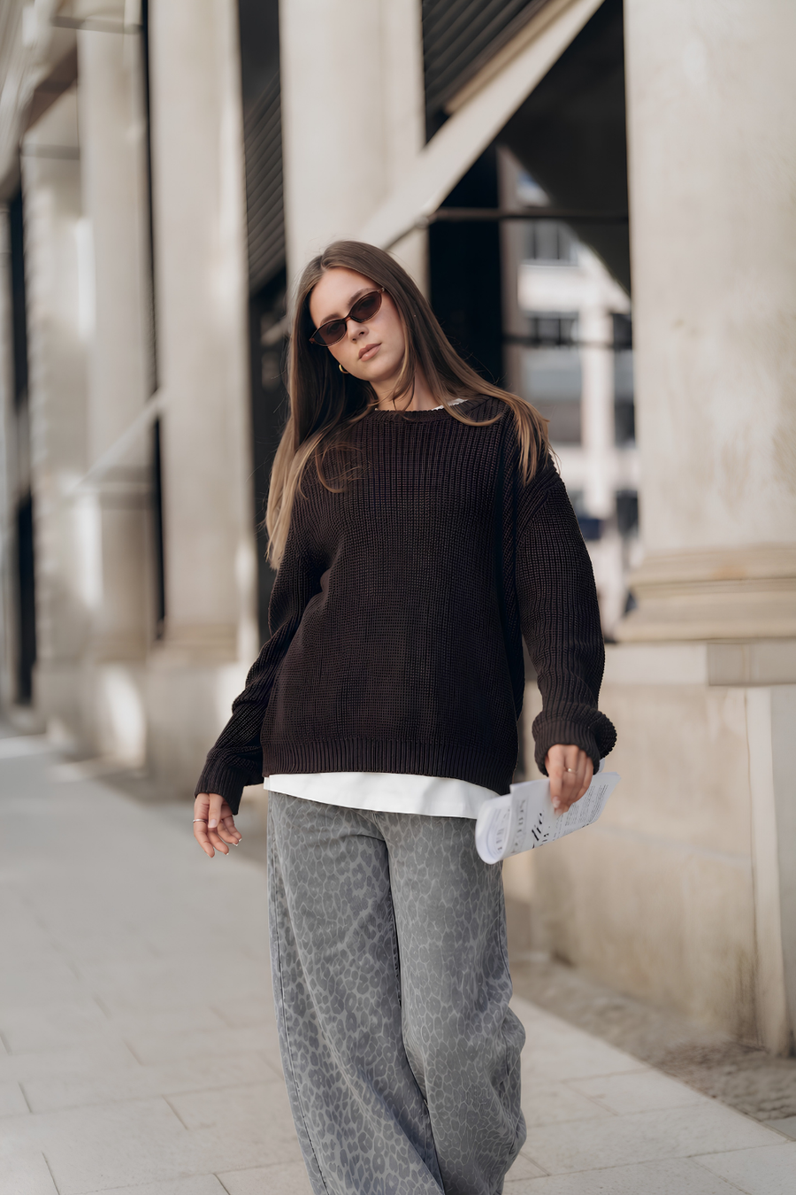 Graue Jeans YOSIE mit weitem Bein und Leo-Print an Model gestylt mit Pullover COSIMA in Dunkelbraun und Oversized T-Shirt ALL TIME BASIC in Weiß.